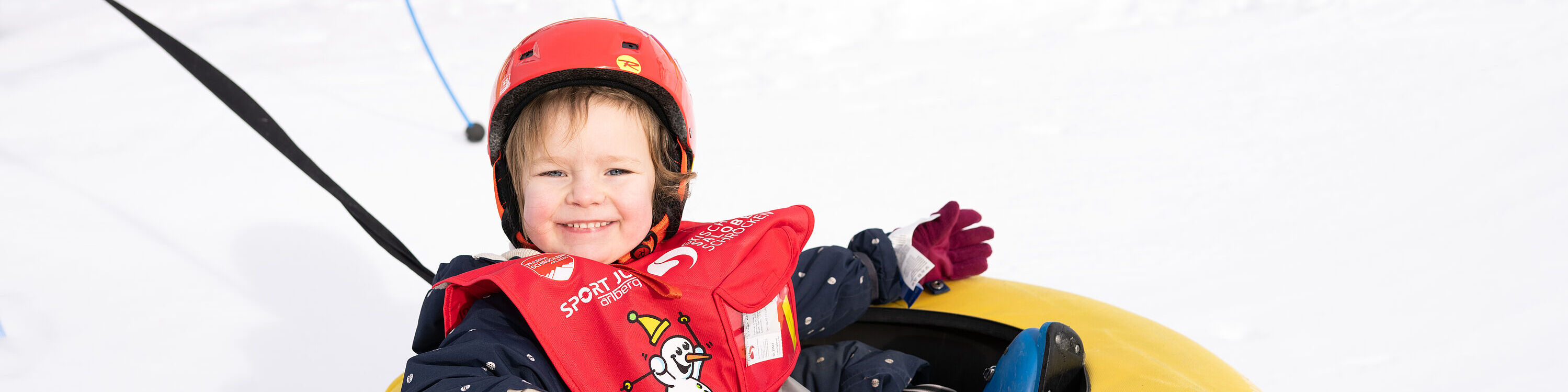 Ein Kleinkind mit roten Helm sitzt lächelnd in einem Gummireifen-Karussell im Kinderland