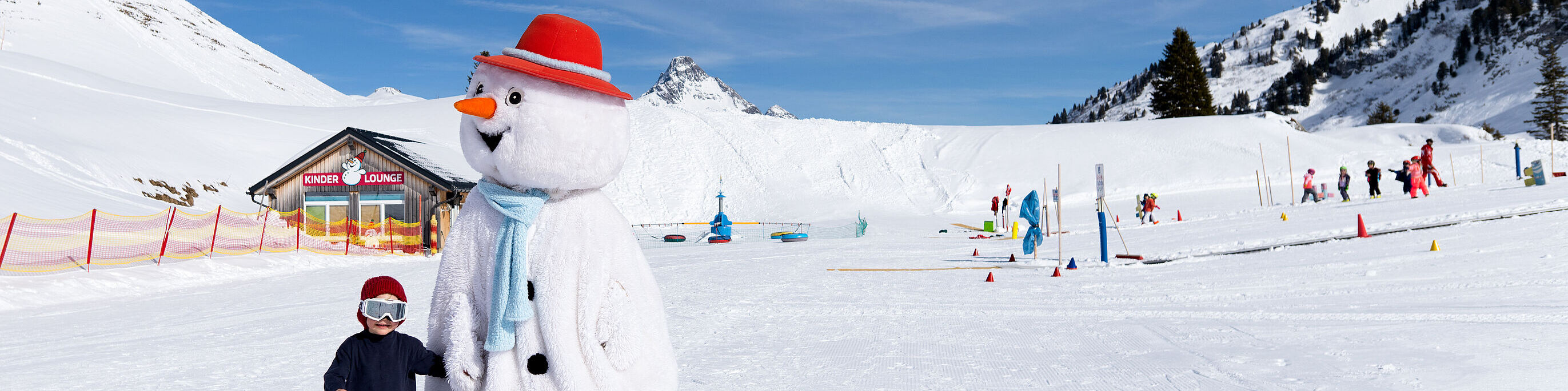 Een kind loopt hand in hand met de sneeuwpopmascotte Pauli in het Kinderland