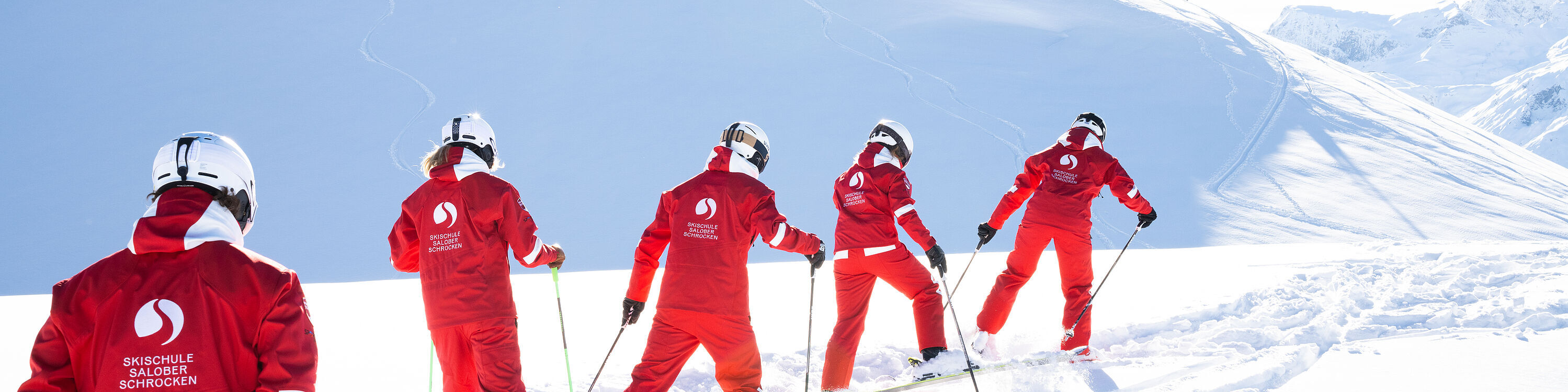 5 Skilehrerinnen und Skilehrer bahnen sich auf Skiern ihren Weg durch den flachen Tiefschnee
