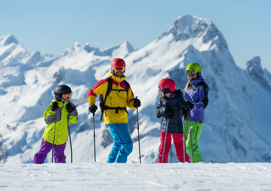 Een gezin van vier staat lachend op de piste met een besneeuwd bergpanorama achter hen