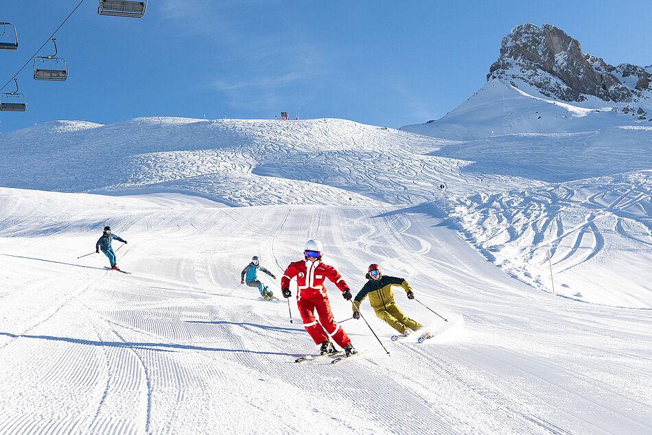 Eine fortgeschrittene Skikurs-Gruppe fährt ihrem Skilehrer in lässigen Schwüngen nach