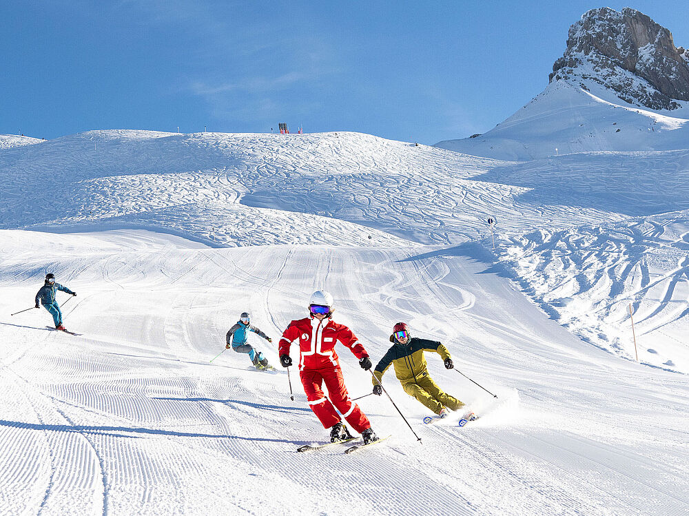 Eine fortgeschrittene Skikurs-Gruppe fährt ihrem Skilehrer in lässigen Schwüngen nach