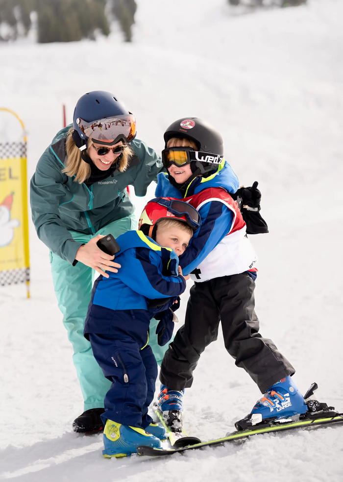 A child is hugging another child who’s on skis