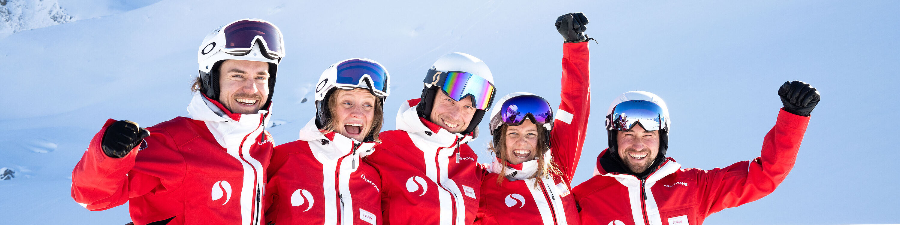 Vijf skileraren in rode skipakken steken hun gebalde vuisten in de lucht en lachen