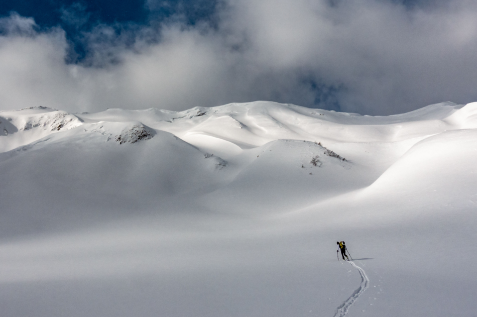 Ein Skitourengeher zieht seine Spur in einsamer, verschneiter Landschaft