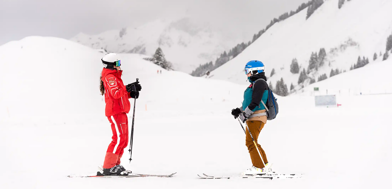Een skilerares van de skischool Salober-Schröcken en een jonge cursist staan tegenover elkaar op de piste en praten met elkaar.
