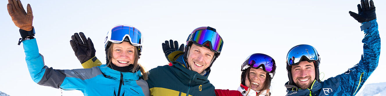 Vier erwachsene Skifahrer winken in die Kamera