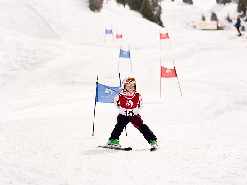 Een deelneemster aan de skiwedstrijd komt in sneeuwploeg over de finish en lacht