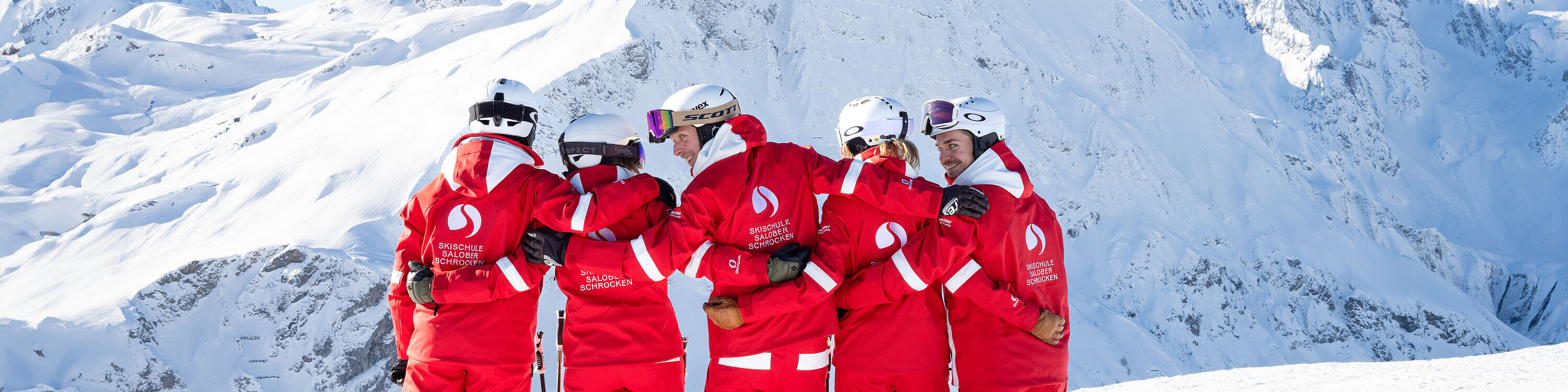 With their backs to the camera, a group of ski instructors are standing arm in arm