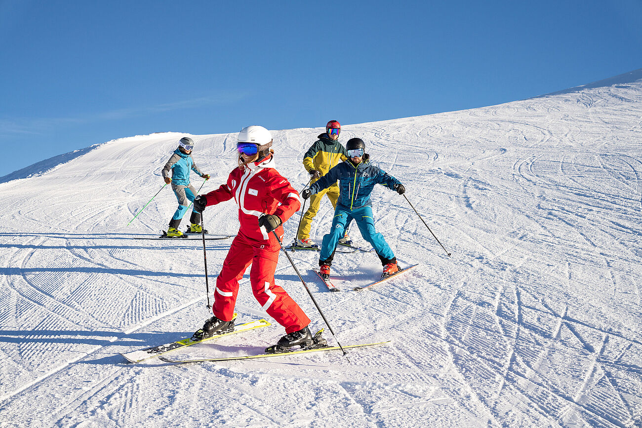 Drei Skifahrer fahren ihrer Skilehrerin auf der Piste im Pflug nach