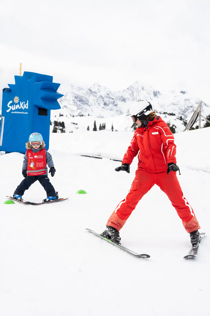 Eine Skilehrerin zeigt einem Kind beim Skikurs, wie man Pflug fährt