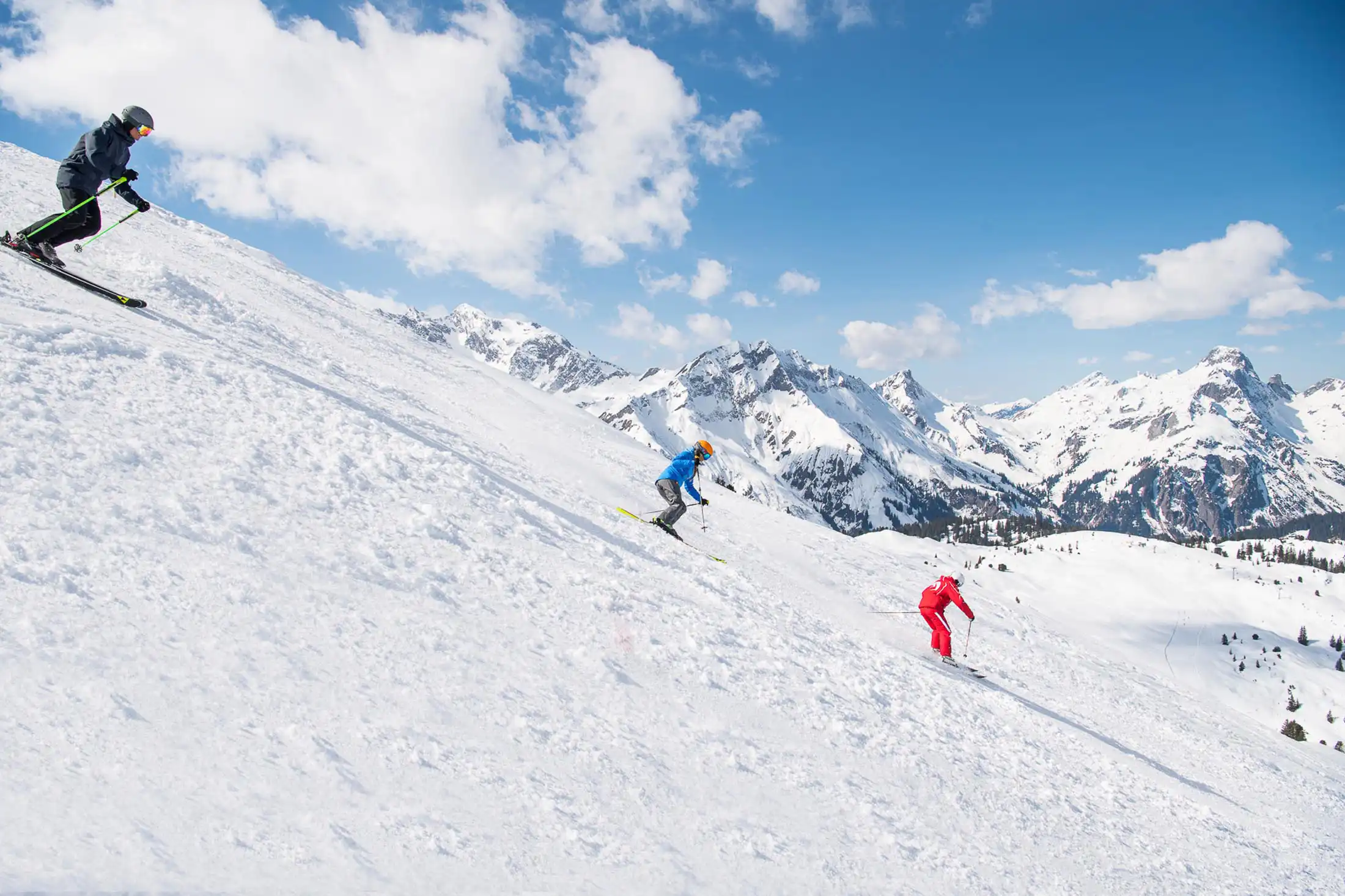 Twee deelnemers aan de skicursus volgen een skileraar van de skischool Salober-Schröcken in bochten op de piste