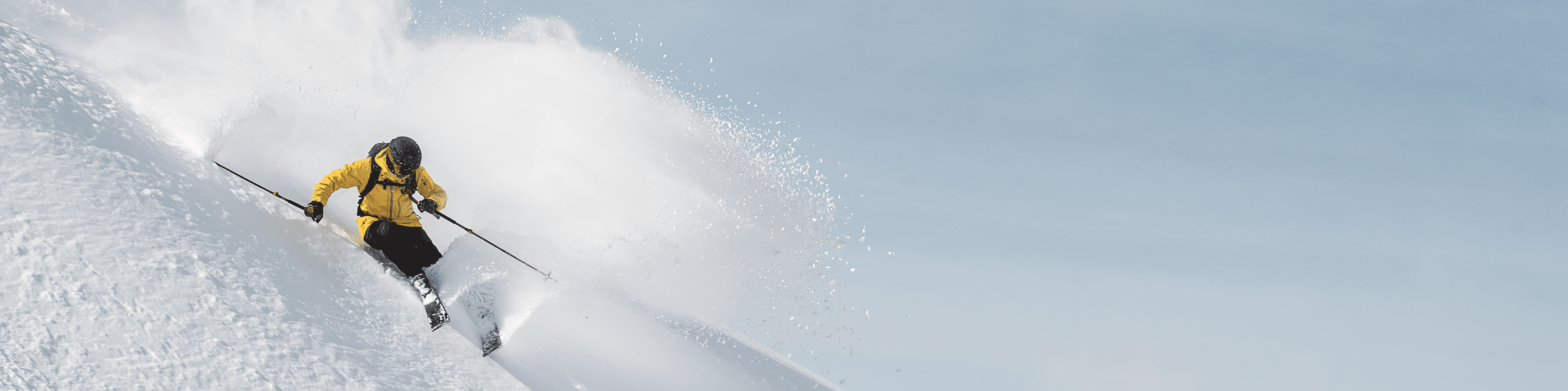 A freerider with a yellow jacket is zooming down a powder snow slope