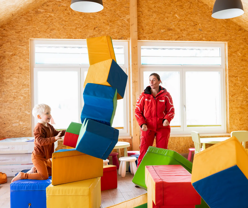 In de indoor speelzone stoot een kind een toren van zachte speelkubussen om