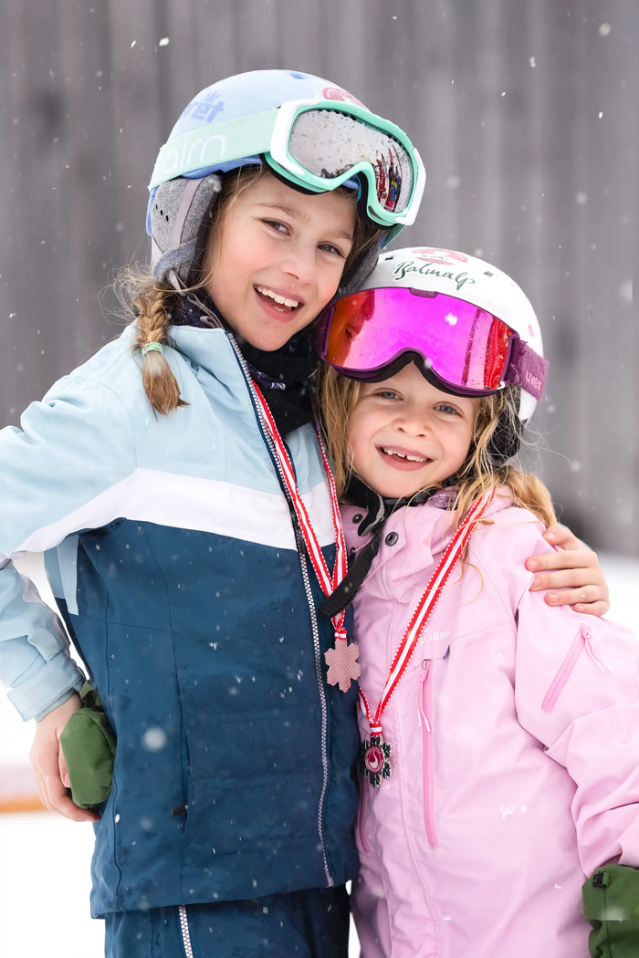 Two girls, arm in arm, proudly displaying their ski racing medals at the awards ceremony