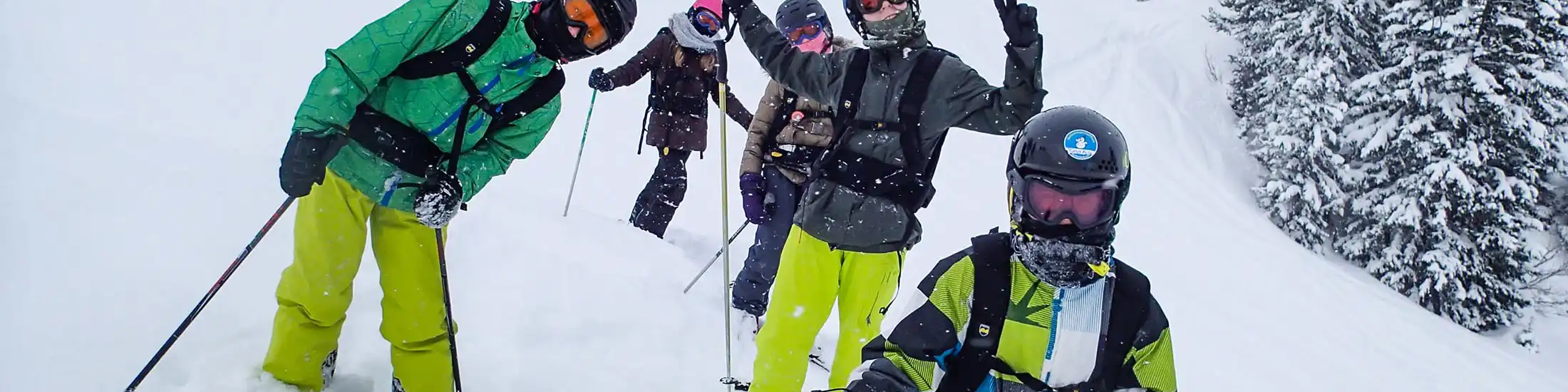 Vijf jongeren in skipakken, met skihelmen en skibrillen staan in de diepe sneeuw en poseren voor de camera