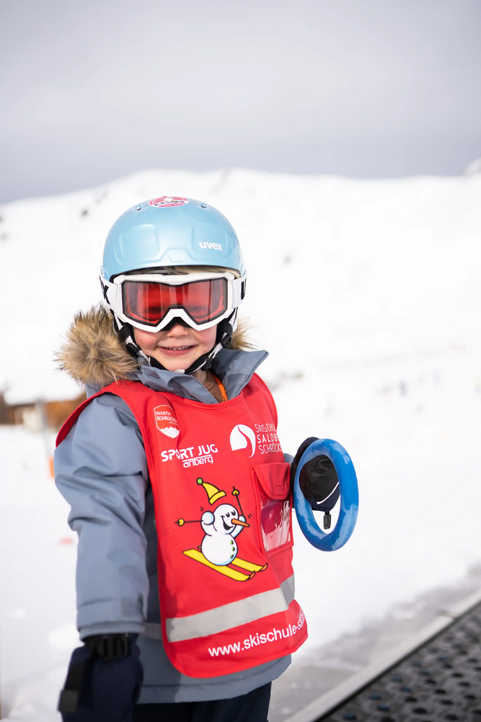 Ein Kind in Ski-Ausrüstung steht lächelnd auf dem Zauberteppich im Kinderland