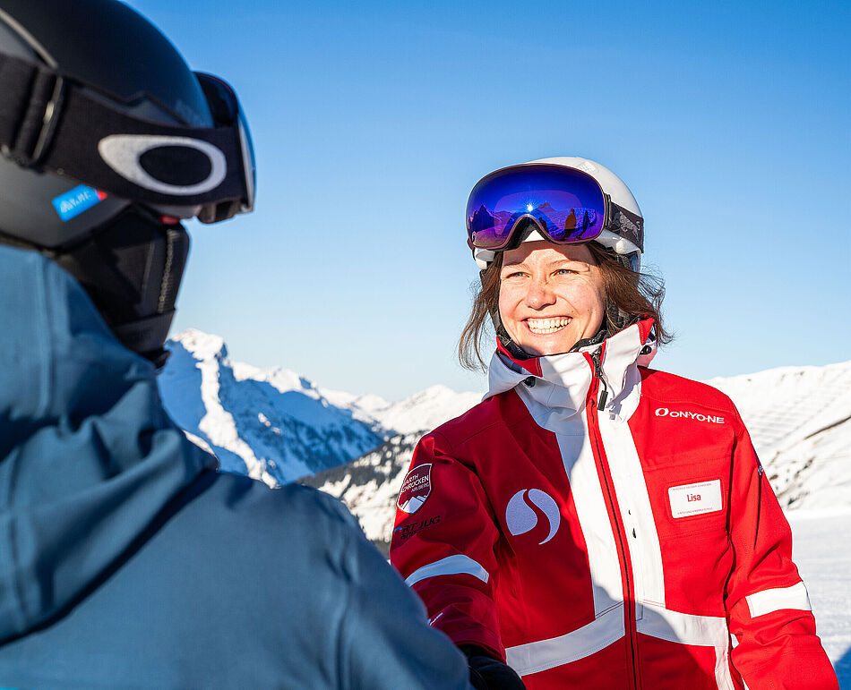 Skilehrerin Marie schüttelt einem Skikurs-Teilnehmer lächelnd die Hand