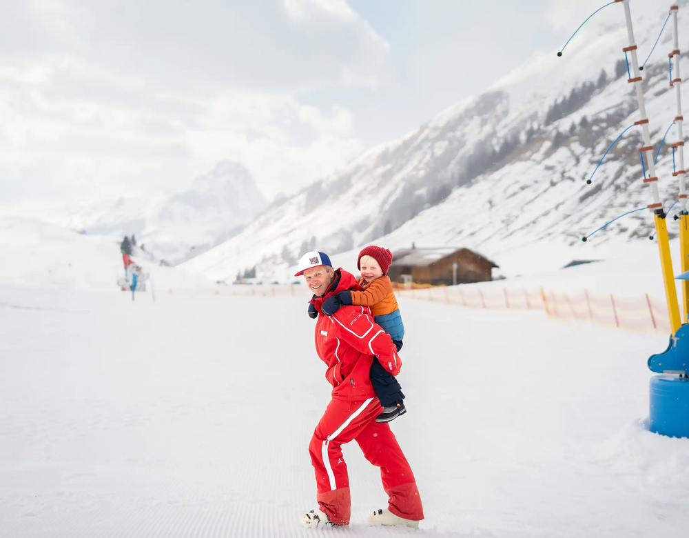 Skischulleiter Daniel nimmt ein Kind im Kinderland Huckepack
