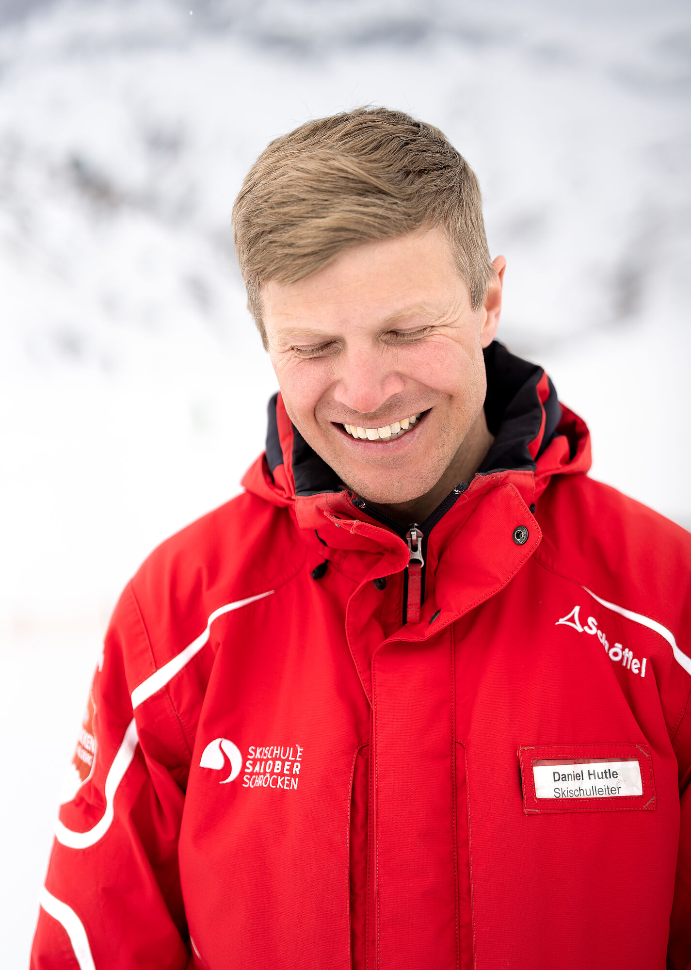 Daniel, the ski school manager, grins broadly into the camera, looking down as he does so